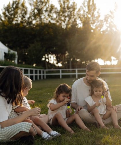 Family sitting on grass enjoying leisure time outdoors, with sun setting in the background.