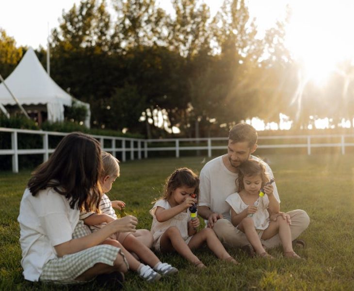 Family sitting on grass enjoying leisure time outdoors, with sun setting in the background.